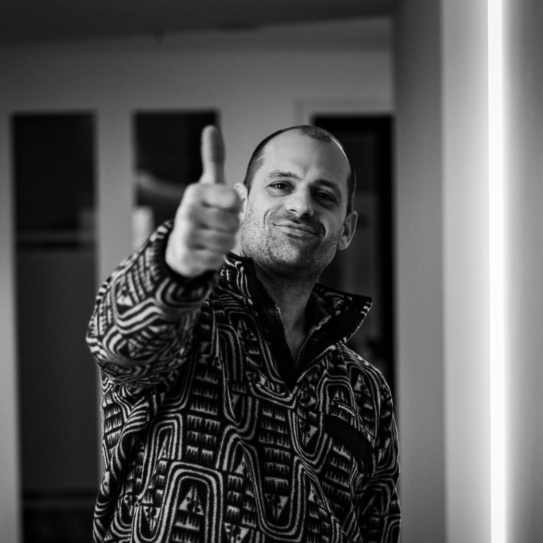 Mitarbeiter der Zahnarztpraxis Chiemgau Lacht zeigt eine Daumen-hoch-Geste im Praxisbereich